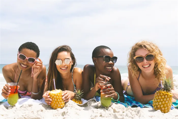 Четыре девушки с разным фототипом на пляже пьют коктейли