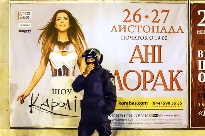 Одинокий полицейский в шлеме стоит на фоне плаката концерта Ани Лорак