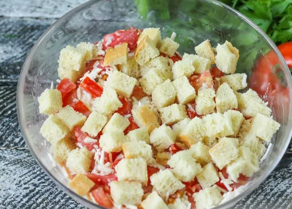 Салат с помидорами, плавленым сыром и сухариками в стеклянной миске на столе