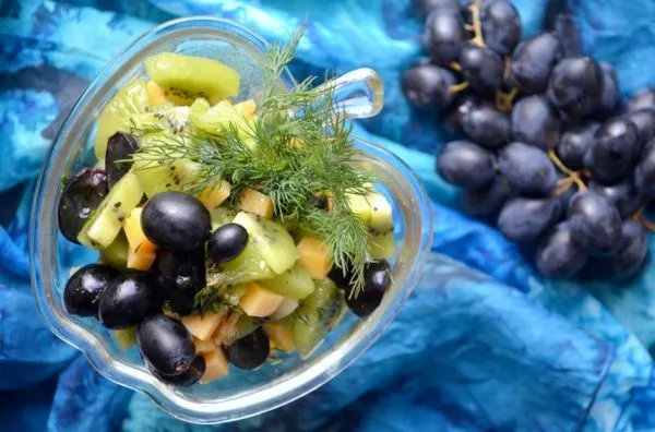 Салат из киви и винограда с сыром и укропом в красивом порционном салатнике на столе с гроздью винограда