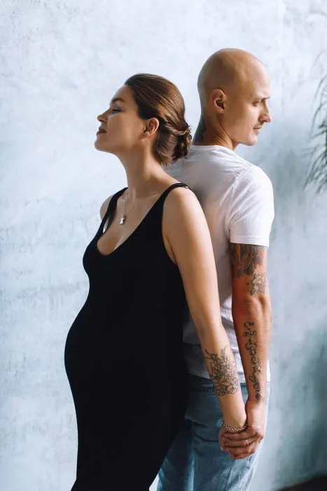 Беременная женщина стоит спиной к спине с мужем